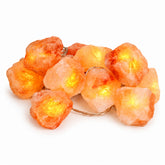 Zen Himalayan Salt Stones with LED String Light; Twelve Himalayan salt stones with warm LED lighting; Natural salt stones arranged with a battery-powered light string; Illuminated Himalayan salt stones on a bedroom shelf; Himalayan salt stones glowing beside indoor plants; LED string woven around natural salt stones; Himalayan salt stone light display in a meditation space; Zen Himalayan Salt Stones product packaging.
