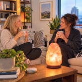 Use only descriptions that match the image shown: Hand-carved Himalayan salt lamp with natural wood base; Himalayan salt lamp emitting a warm glow; Natural Himalayan salt lamp with unique shape and colour; Small Himalayan salt lamp for a bedside table; Himalayan salt lamp displayed in a living room; Large Himalayan salt lamp with wood base; Himalayan salt lamp in a meditation space; Himalayan salt lamp with included bulb and AC power cord.