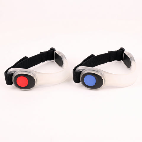 Use only descriptions that match the image shown: LED Safety Arm Bands 2-pack; LED arm band with steady illumination; LED arm band in flashing mode; Adjustable hook-and-loop strap on an LED arm band; Reflective pull tab on the LED safety arm band; LED Safety Arm Band worn while running; LED arm band worn while cycling; CR2032 battery compartment on the LED arm band