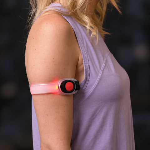 Use only descriptions that match the image shown: LED Safety Arm Bands 2-pack; LED arm band with steady illumination; LED arm band in flashing mode; Adjustable hook-and-loop strap on an LED arm band; Reflective pull tab on the LED safety arm band; LED Safety Arm Band worn while running; LED arm band worn while cycling; CR2032 battery compartment on the LED arm band