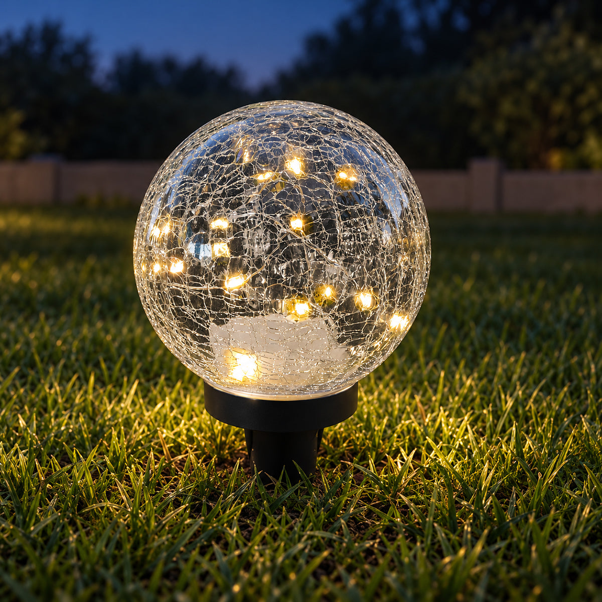 Use only descriptions that match the image shown: Solar Faerie LED Globe with detachable garden stake; Hand-blown crackle glass solar globe; Solar Faerie LED Globe illuminated at dusk; Crackle glass globe displayed in a garden; Solar LED globe on a patio table without its stake; Close-up of the Solar Faerie LED Globe crackle glass; Medium Solar Faerie LED Globe, 15 cm diameter.
